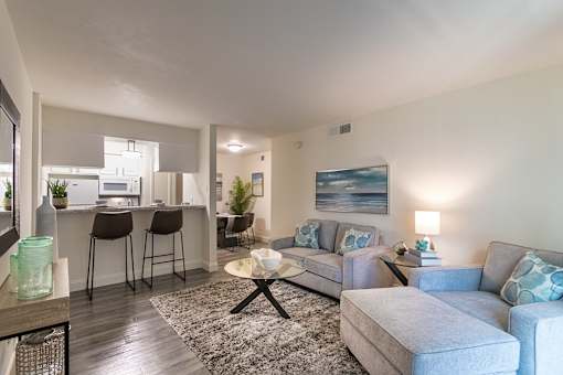 Open living room with sectional seating, wood-look flooring, and breakfast bar in the 558-square-foot 1 Bedroom, 1 Bath A