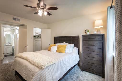 A bedroom with a bed, dresser, and ceiling fan.