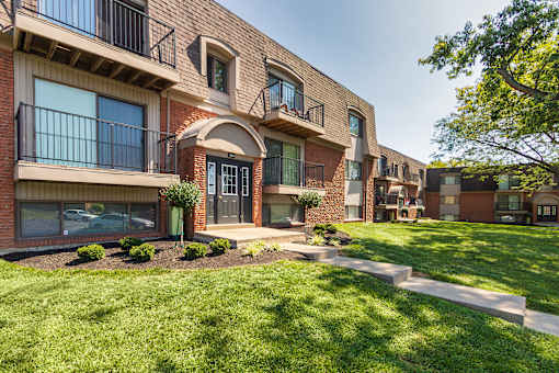 Brick apartment building with balconies, arched entry, and landscaped grounds at Village East Apartments