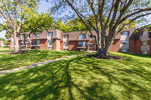 Open green space with mature trees and apartment buildings at Village East Apartments