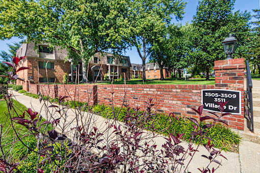 Brick wall with address sign grassy, shaded courtyard between brick buildings at Village East Apartments