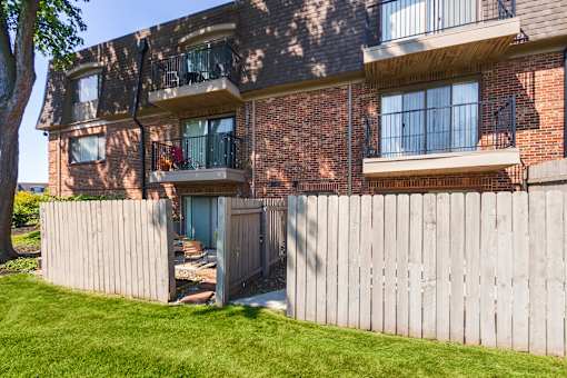 Apartment building exterior with private patio fencing and landscaped lawn at Village East Apartments