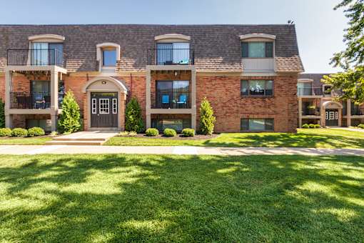 Apartment building with balconies, arched entry, and green lawn at Village East Apartments