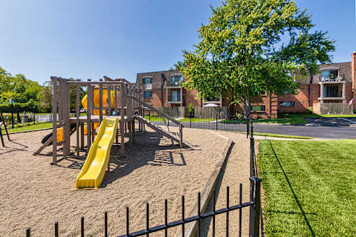 Playground and fenced recreation area with apartment buildings in the background at Village East Apartments