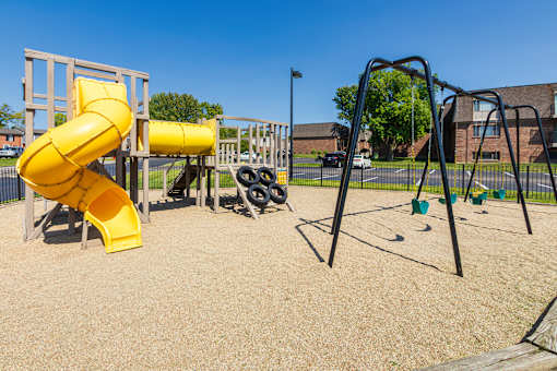 Playground with spiral slide, swings, and open play area at Village East Apartments