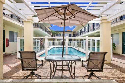 a patio with a pool and a table with chairs and an umbrella at Olive Tree Apartments, Torrance, CA 90503