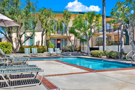 a swimming pool with chairs and a building in the background at Camino de Oro Apartments, California, 90505