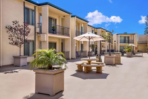 a courtyard with tables and umbrellas in front of apartments at Casa Del Amo Apartments, Torrance