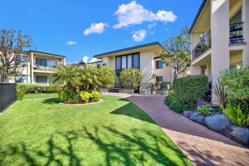 a yard with grass and palm trees in front of an apartment building at Casa Del Amo Apartments, Torrance California