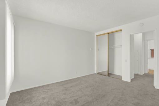 an empty living room with white walls and a door to a closet at Copa Triana Apartments, Torrance, CA
