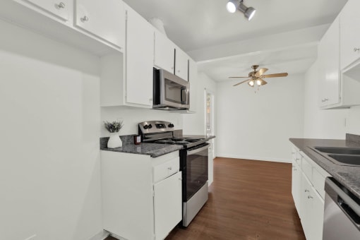 a kitchen with white cabinets and a stove and a microwave at Copa Triana Apartments, Torrance California
