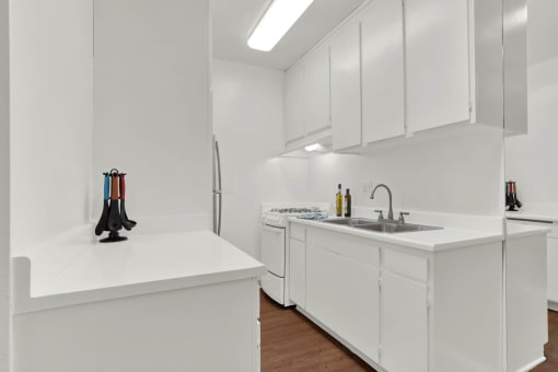 a kitchen with white cabinets and a sink and a refrigerator at Olive Tree Apartments, Torrance, 90503