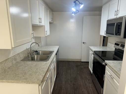 A kitchen with white cabinets and a marble countertop. at Copa Triana Apartments, Torrance