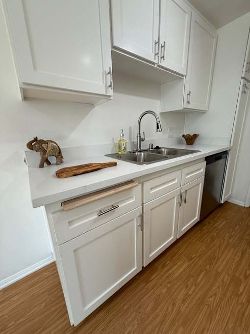 A kitchen with white cabinets and wooden floors.