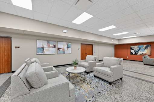 A spacious waiting room with a grey sofa, two chairs, and a coffee table.