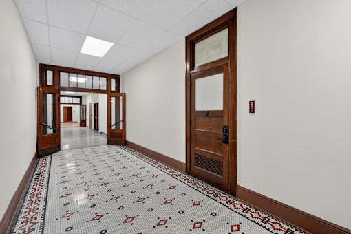 A hallway with a tiled floor and a brown door.