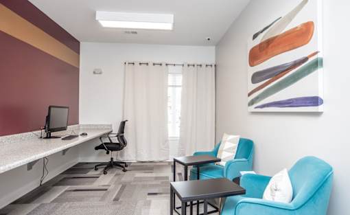 A room with a desk, chairs, and a painting on the wall.