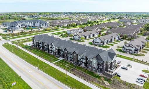 A large, modern apartment complex is surrounded by smaller houses and a road with cars.