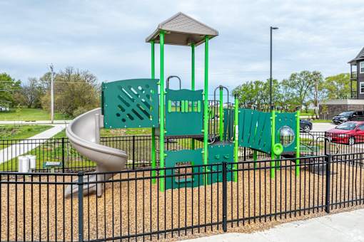 A playground with a green slide and a black fence.