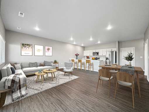 A modern living room with a grey sofa, wooden chairs, and a dining table.
