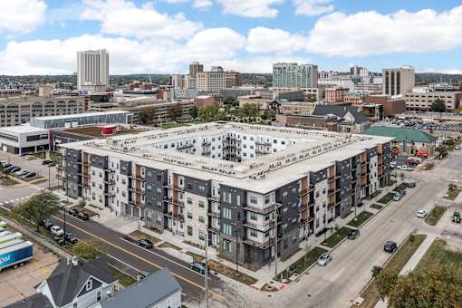 A large apartment complex is surrounded by a parking lot and other buildings.