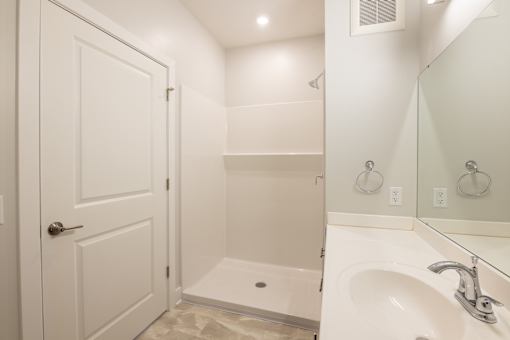 A white bathroom with a door, sink, and mirror.