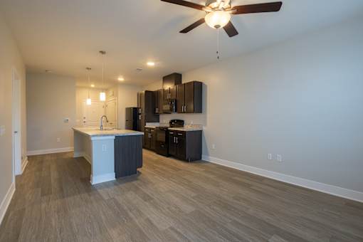 A room with a ceiling fan and a kitchen area with a counter and cabinets.