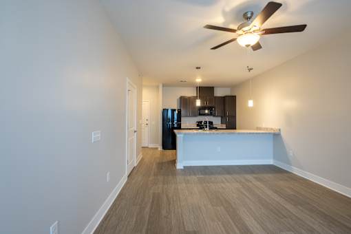 A room with a ceiling fan and a kitchen area in the background.