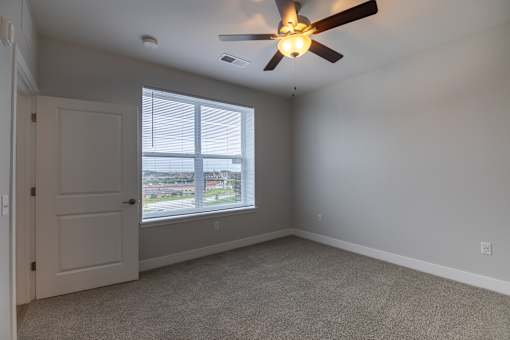 A room with a ceiling fan and a window overlooking a parking lot.