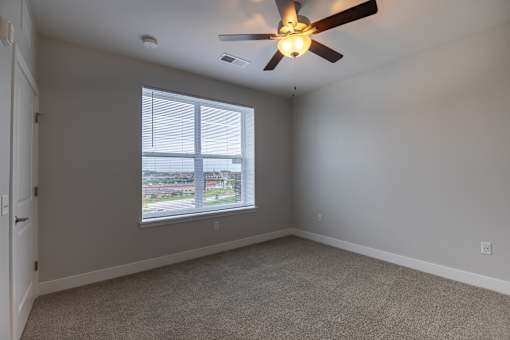 A room with a ceiling fan and a window overlooking a parking lot.