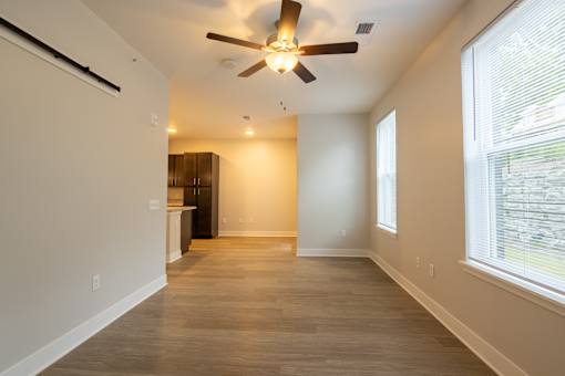 A room with a ceiling fan and light fixture, wooden flooring, and a window with blinds.