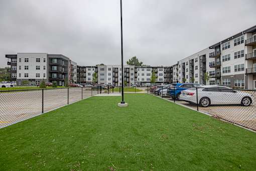 A grassy area in front of apartment buildings with cars parked in the background.