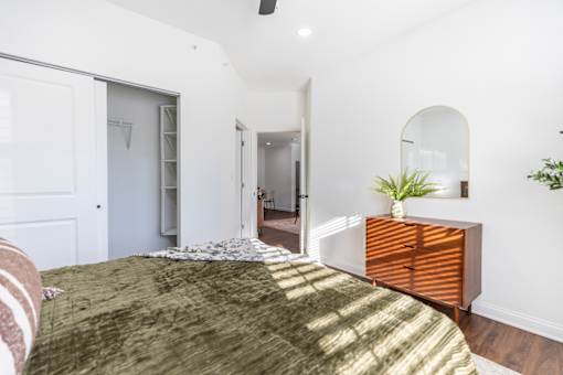 A bedroom with a bed in the foreground and a dresser with a mirror above it.
