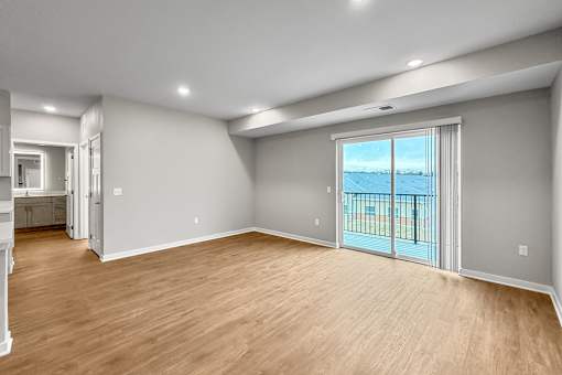 A spacious room with wooden flooring and a sliding glass door leading to a balcony.
