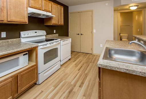 A kitchen with wooden cabinets and a white stove top oven at Cedarbrooke Place , Norwalk, IA, 50211