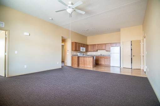 A spacious room with a ceiling fan and a kitchen area in the background.at Cottages at Johnston Commons, Iowa, 50131