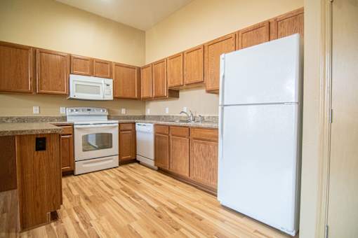 A kitchen with wooden cabinets and a white refrigerator.at Cottages at Johnston Commons, Iowa, 50131