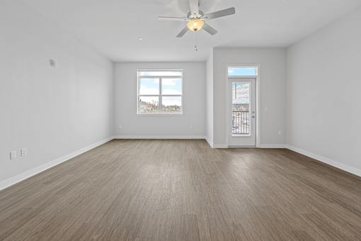 A room with a ceiling fan and light, hardwood floors, and a window with a view of the outside.