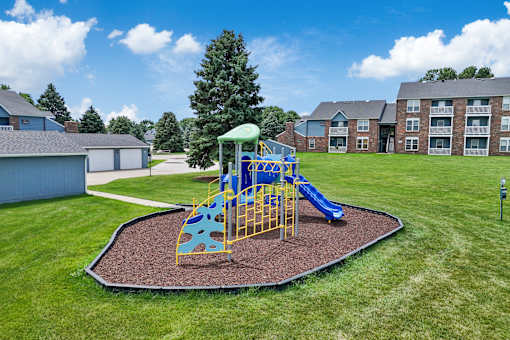 A playground with a yellow and blue slide in the middle of a grassy area.