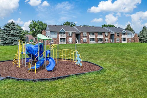 A playground with a blue slide and yellow safety barriers in front of a brick building.
