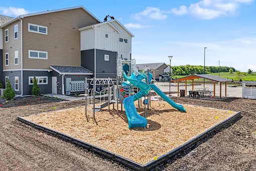 A playground with a blue slide in the foreground and houses in the background.