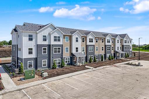 A row of new townhouses with a parking lot in front.