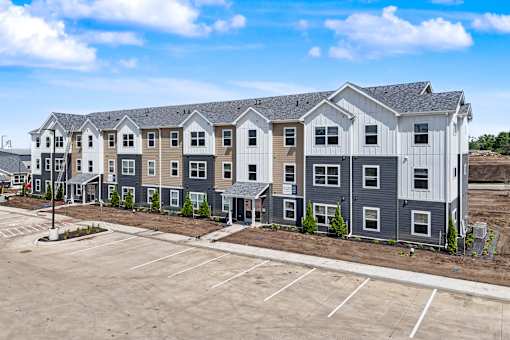 A row of new townhouses with a parking lot in front.
