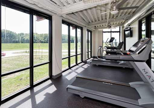 A treadmill in a room with a ceiling fan and large windows. at Eagle View Lofts, Iowa, 50309