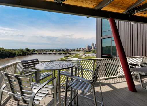 A table and chairs are set up on a deck overlooking a river. at Eagle View Lofts, Des Moines, 50309