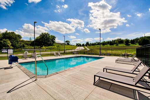 A pool surrounded by a concrete patio and lounge chairs.