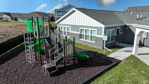 A playground with a green slide and a grey house in the background.