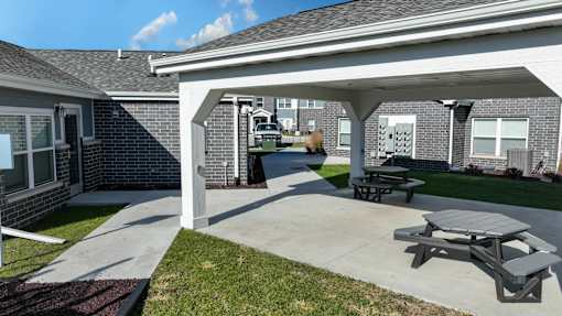 A patio area with a picnic table and benches under a covered section of a building.