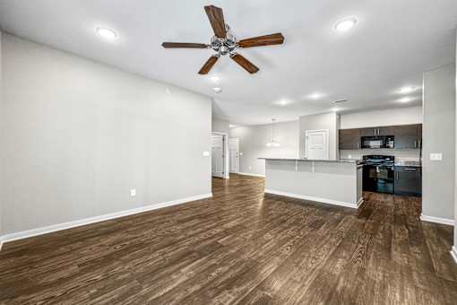 an empty living room with a ceiling fan and a kitchen at The Barclay Apartments, Altoona, IA, 50009