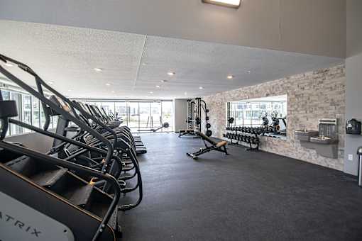A gym with a row of treadmills on the left and a row of exercise bikes on the right.at Linc, Des Moines, 50309  